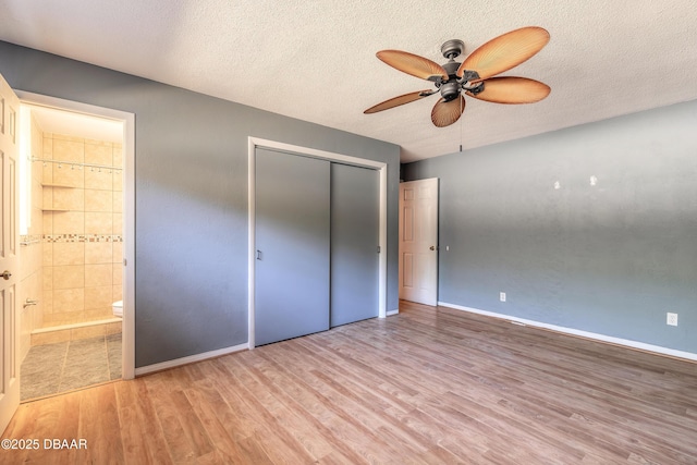 unfurnished bedroom featuring ceiling fan, connected bathroom, light wood-type flooring, a closet, and a textured ceiling