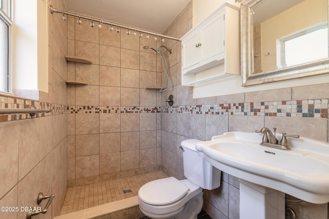 bathroom with toilet, sink, and tiled shower