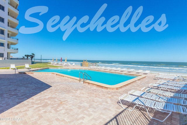 view of swimming pool with a patio, a beach view, and a water view