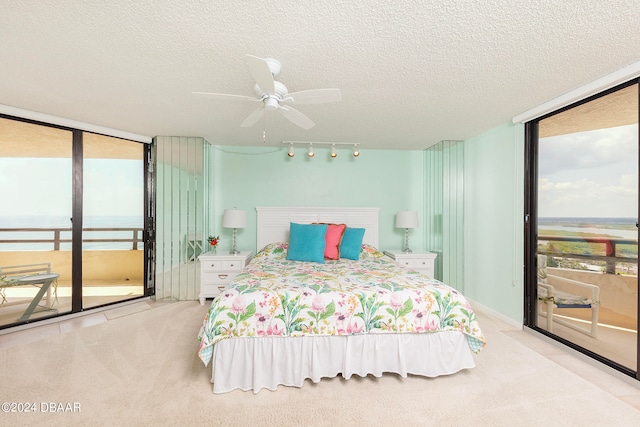 bedroom featuring a textured ceiling, light carpet, a wall of windows, rail lighting, and ceiling fan