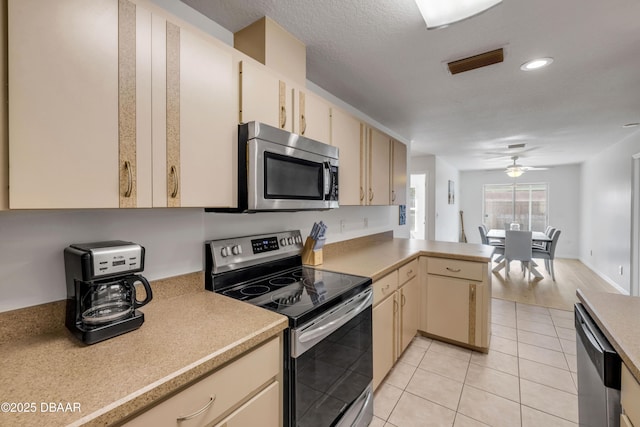 805 Spruce St, New Smyrna Beach, FL 32168 - kitchen with appliances with stainless steel finishes, a peninsula, cream cabinetry, light tile patterned floors, and light countertops