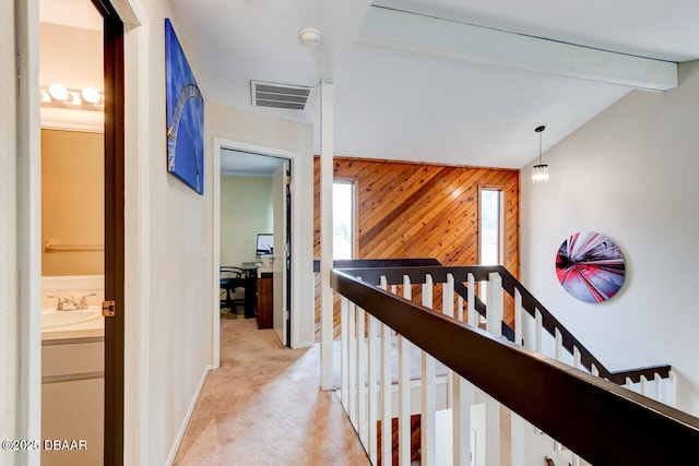 hallway with visible vents, vaulted ceiling with beams, wood walls, light carpet, and an upstairs landing