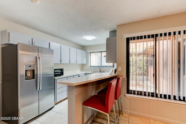 kitchen with light tile patterned floors, a peninsula, light countertops, stainless steel refrigerator with ice dispenser, and black microwave