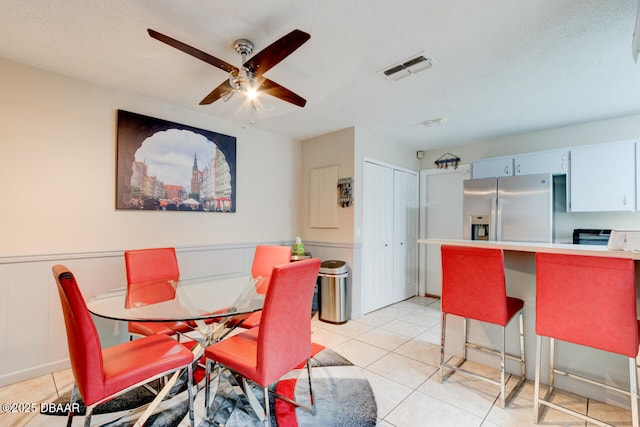 dining room with light tile patterned flooring, visible vents, wainscoting, and a ceiling fan