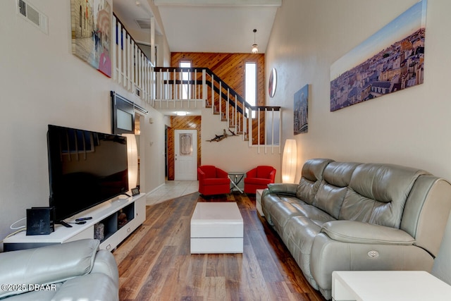 living area featuring wooden walls, wood finished floors, visible vents, a high ceiling, and stairs