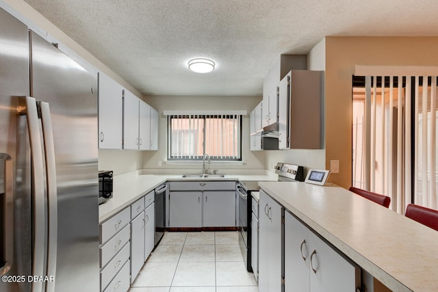 kitchen with under cabinet range hood, light countertops, light tile patterned floors, stainless steel appliances, and a sink