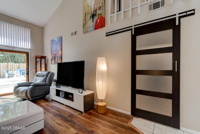 living area with wood finished floors, baseboards, visible vents, high vaulted ceiling, and a barn door