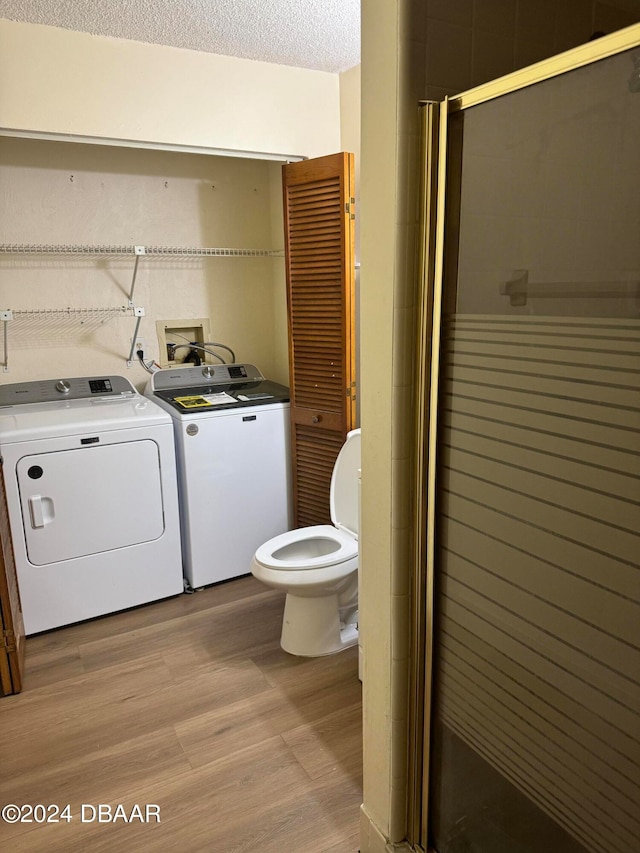 bathroom with wood-type flooring, a shower with door, washer and clothes dryer, a textured ceiling, and toilet