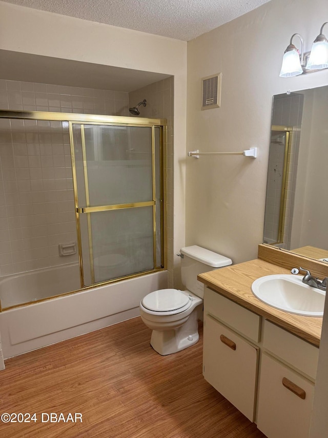 full bathroom featuring wood-type flooring, toilet, bath / shower combo with glass door, a textured ceiling, and vanity