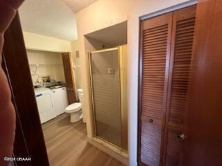 bathroom featuring wood-type flooring, toilet, a shower with shower door, and independent washer and dryer