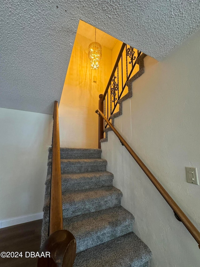 stairs featuring hardwood / wood-style flooring, a textured ceiling, and a notable chandelier