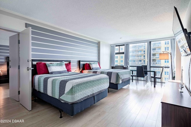 bedroom with a textured ceiling, a wall of windows, and light hardwood / wood-style flooring