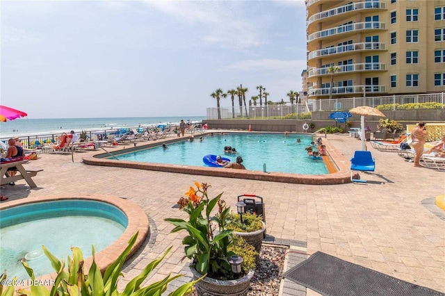 view of swimming pool with a jacuzzi, a water view, and a patio area