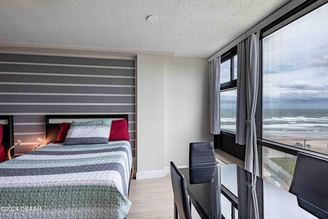 bedroom with light wood-type flooring, a water view, and a textured ceiling