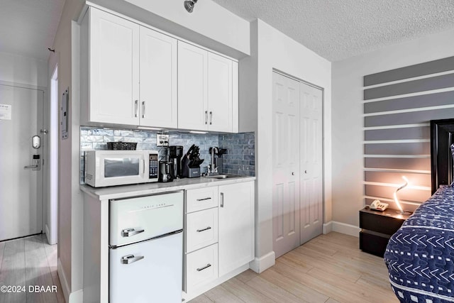 kitchen with white cabinetry, light wood-type flooring, sink, and a textured ceiling