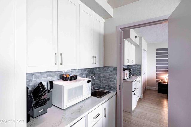 kitchen with white cabinets, light wood-type flooring, a textured ceiling, and backsplash