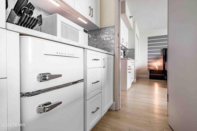 kitchen with white cabinetry, a textured ceiling, backsplash, and light hardwood / wood-style flooring