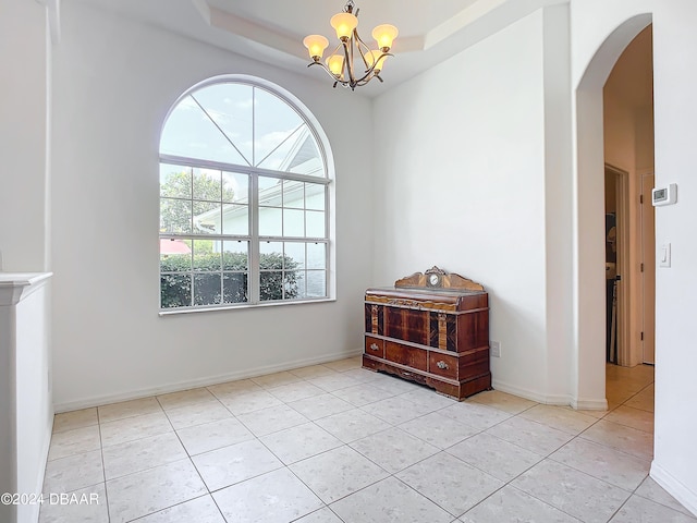 tiled empty room featuring a raised ceiling and an inviting chandelier