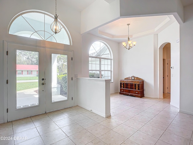 tiled foyer entrance featuring plenty of natural light, french doors, a tray ceiling, and an inviting chandelier