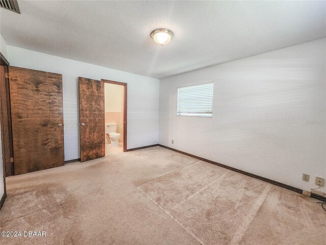 unfurnished bedroom featuring ensuite bathroom, a textured ceiling, and carpet flooring