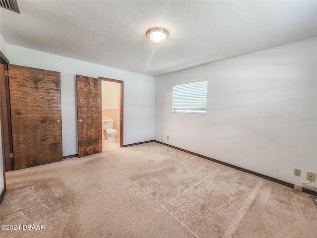 unfurnished bedroom with a textured ceiling, carpet, and ensuite bath