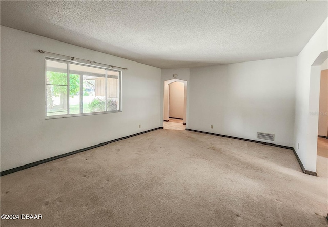 empty room with light colored carpet and a textured ceiling