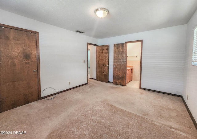 unfurnished bedroom featuring a textured ceiling, light carpet, and ensuite bath