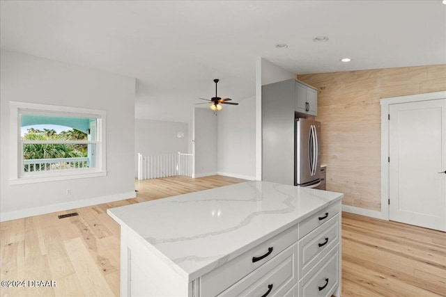 kitchen with stainless steel fridge, light wood-type flooring, light stone counters, ceiling fan, and a kitchen island