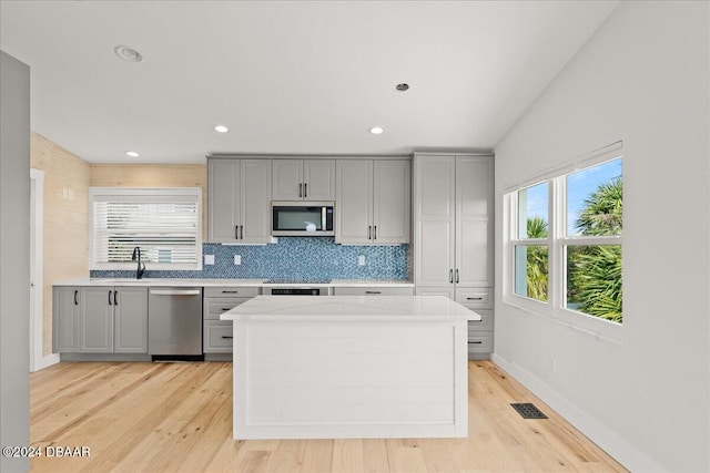 kitchen with gray cabinetry, light hardwood / wood-style flooring, backsplash, vaulted ceiling, and appliances with stainless steel finishes