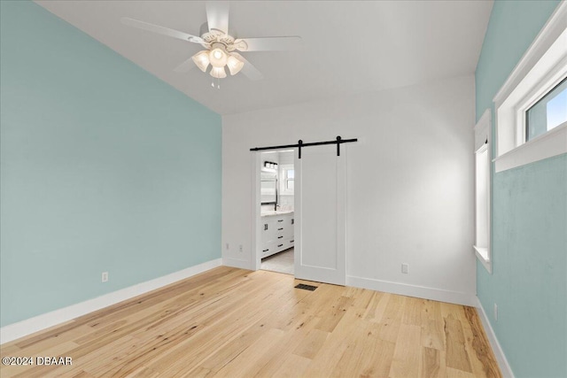 spare room featuring light wood-type flooring, plenty of natural light, a barn door, and ceiling fan