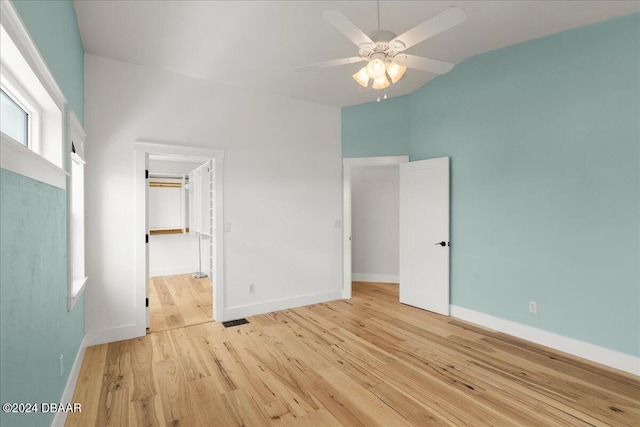 unfurnished bedroom with a walk in closet, vaulted ceiling, ceiling fan, light wood-type flooring, and a closet