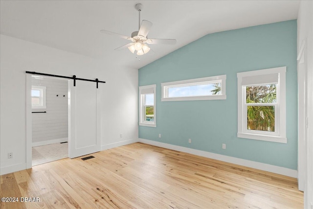 unfurnished bedroom with a barn door, light hardwood / wood-style flooring, ensuite bath, and multiple windows