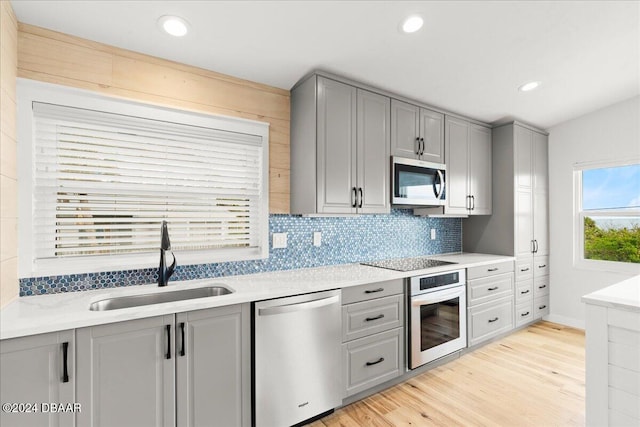 kitchen featuring gray cabinetry, sink, stainless steel appliances, tasteful backsplash, and light hardwood / wood-style floors