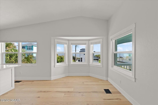 spare room with a healthy amount of sunlight, vaulted ceiling, and light hardwood / wood-style floors