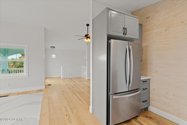 kitchen with light wood-type flooring, wooden walls, stainless steel refrigerator, and gray cabinetry