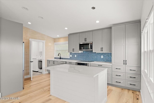 kitchen with appliances with stainless steel finishes, sink, light hardwood / wood-style flooring, a center island, and lofted ceiling