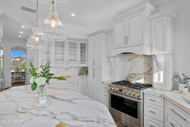 kitchen featuring white cabinetry, light stone counters, backsplash, hanging light fixtures, and stainless steel stove