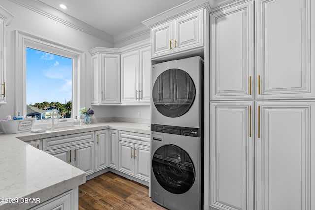 laundry area featuring ornamental molding, stacked washer and dryer, cabinets, sink, and dark wood-type flooring