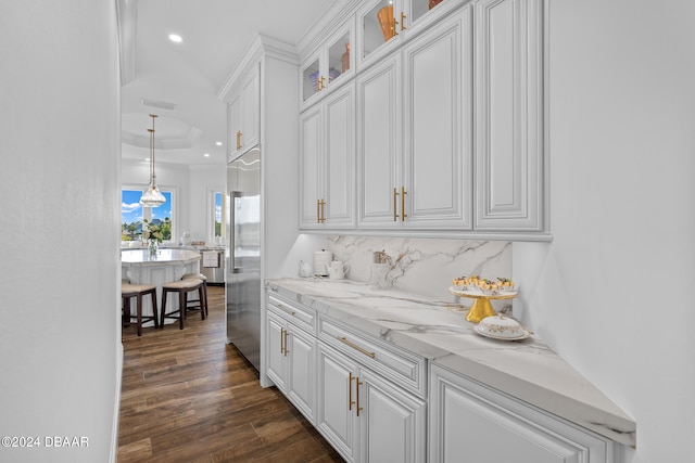 bar featuring dark wood-type flooring, built in fridge, white cabinets, hanging light fixtures, and tasteful backsplash