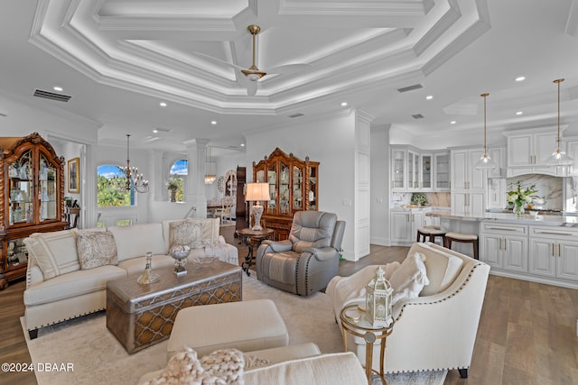 living room featuring ornate columns, ceiling fan with notable chandelier, a raised ceiling, crown molding, and light hardwood / wood-style flooring