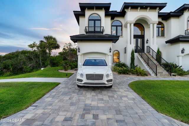 view of front of property featuring a balcony, a garage, and a yard