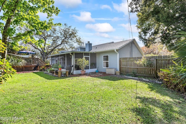 rear view of house featuring a deck, fence, a sunroom, a yard, and a chimney