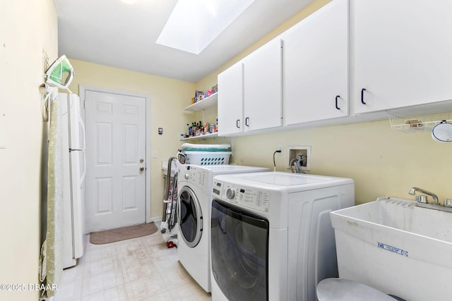 clothes washing area with cabinet space, a skylight, washer and clothes dryer, light floors, and a sink