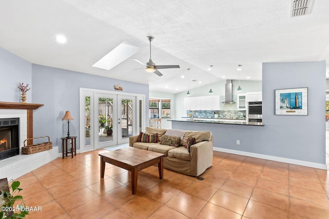 living room featuring light tile patterned floors, baseboards, visible vents, lofted ceiling with skylight, and a brick fireplace