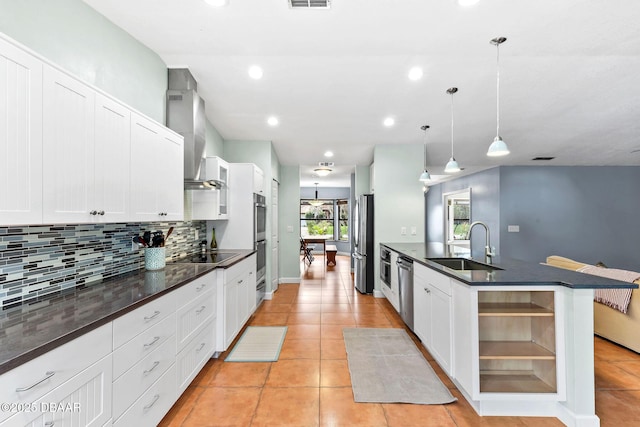 kitchen featuring decorative backsplash, dark countertops, wall chimney exhaust hood, appliances with stainless steel finishes, and a sink