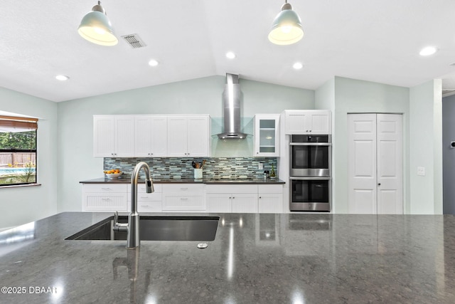 kitchen featuring stainless steel double oven, a sink, visible vents, wall chimney exhaust hood, and tasteful backsplash