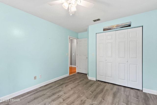 unfurnished bedroom with a closet, wood finished floors, visible vents, and baseboards