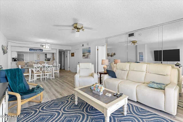 living room with light hardwood / wood-style flooring, a textured ceiling, and ceiling fan