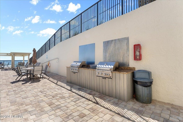 view of patio with area for grilling, a water view, a pergola, and exterior kitchen