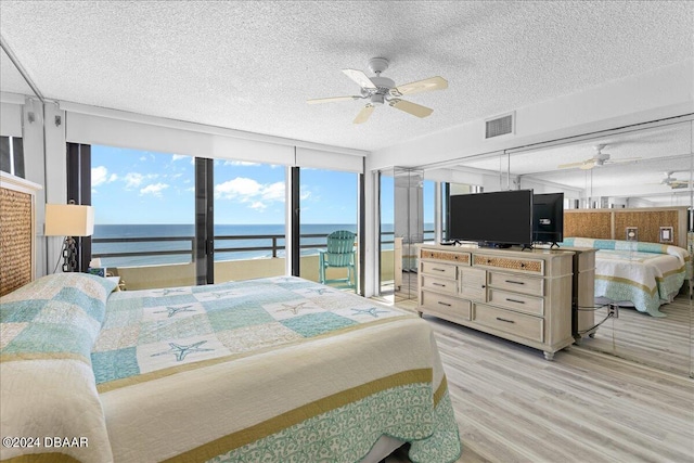 bedroom featuring light hardwood / wood-style floors, access to exterior, a textured ceiling, floor to ceiling windows, and ceiling fan